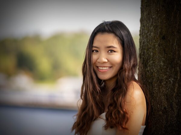 A young woman leaning against a tree.