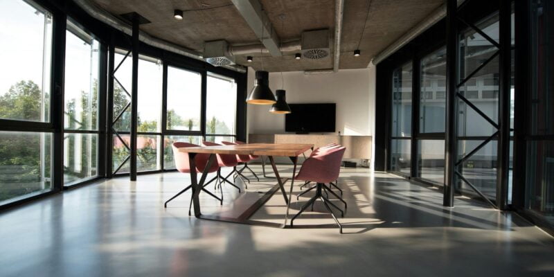 Modern conference room with a long wooden table, contemporary chairs, and large windows providing ample natural light.