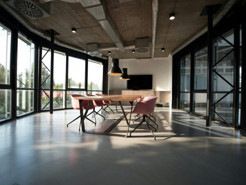 Modern conference room with a long wooden table, contemporary chairs, and large windows providing ample natural light.