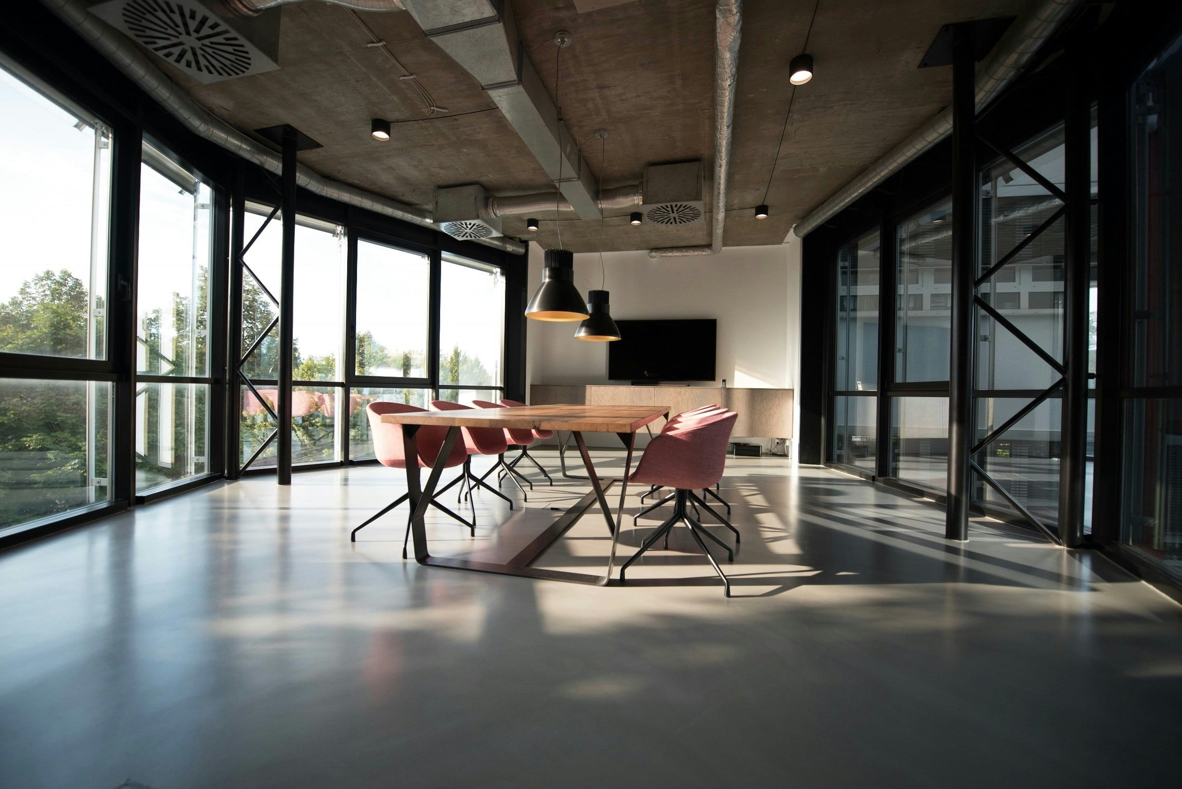 Modern conference room with a long wooden table, contemporary chairs, and large windows providing ample natural light.