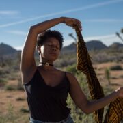 A black woman is holding a scarf in the desert.