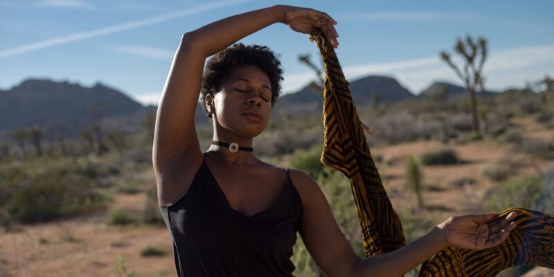 A black woman is holding a scarf in the desert.