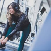 A woman is putting on her headphones in a gym, preparing for a session with the latest Home Workout Innovations.