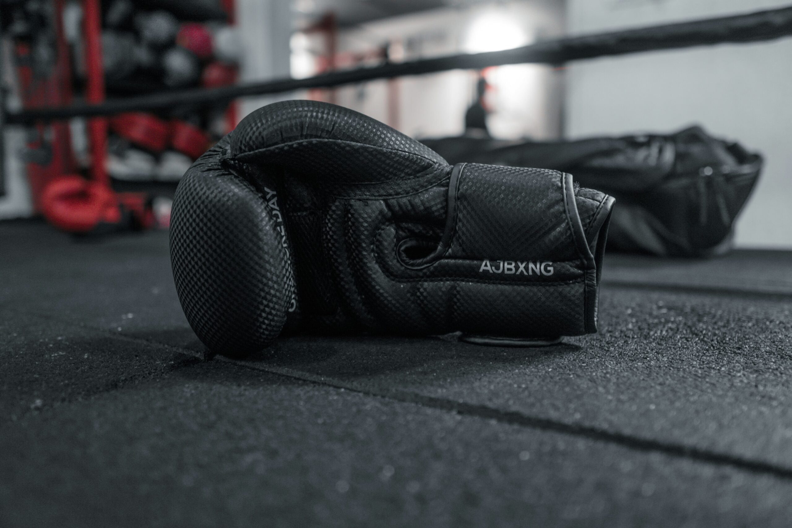 A pair of black boxing gloves from the Liteboxer Fitness Bundle lying on a gym floor with equipment in the background.