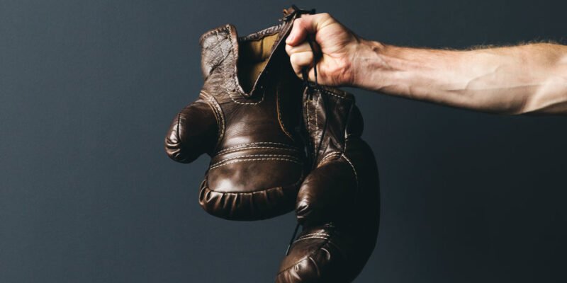 A man holding a pair of boxing gloves on a dark background.