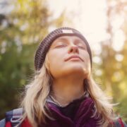 A woman in a beanie looking up at the sun in the woods, contemplating why Facebook is down.