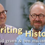 Two men, each wearing glasses, sit and smile in a room with the text "Writing History" and "david grann & ben macintyre" written on the image.