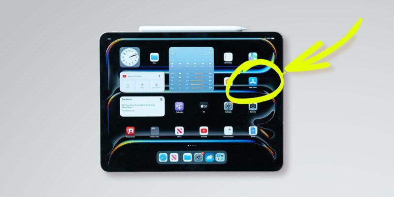 A digital tablet displaying a home screen with various app icons. A yellow arrow highlights the App Store icon on the screen. A white stylus is placed above the tablet.